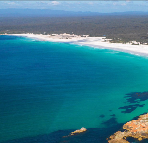 Aerial photo of bright blue ocean and white sandy shoreline.
