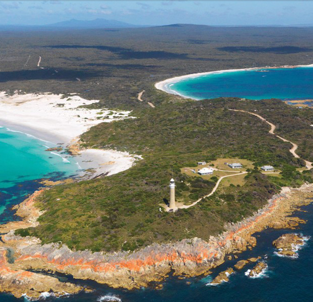 Coastal headland with lighthouse and sandy bays surrounded by clear blue sea.